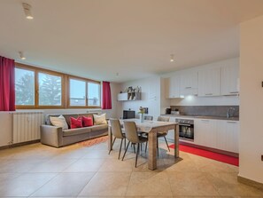 A modern kitchen with white cabinets, a dining area with a table and chairs, a sofa with red cushions, and a window with curtains. - Ciasina Alpina by Interhome (Folgarida)