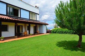 Een twee verdiepingen tellend huis met een overdekte patio, gazon en een pijnbom.