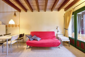 Una habitación con un sofá rojo, sillas blancas, una mesita y una ventana con cortinas.