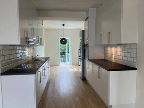 A modern kitchen with white cabinetry, a black countertop, and a view to a balcony. - 3 Bedroom new Flat Close to Oslo Fjord (Bærum)