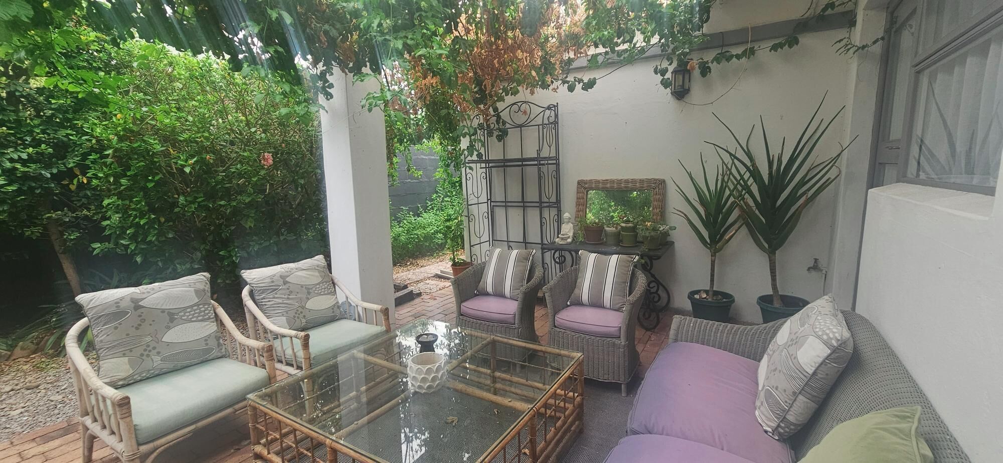 A covered patio with wicker furniture, a glass table, and potted plants.