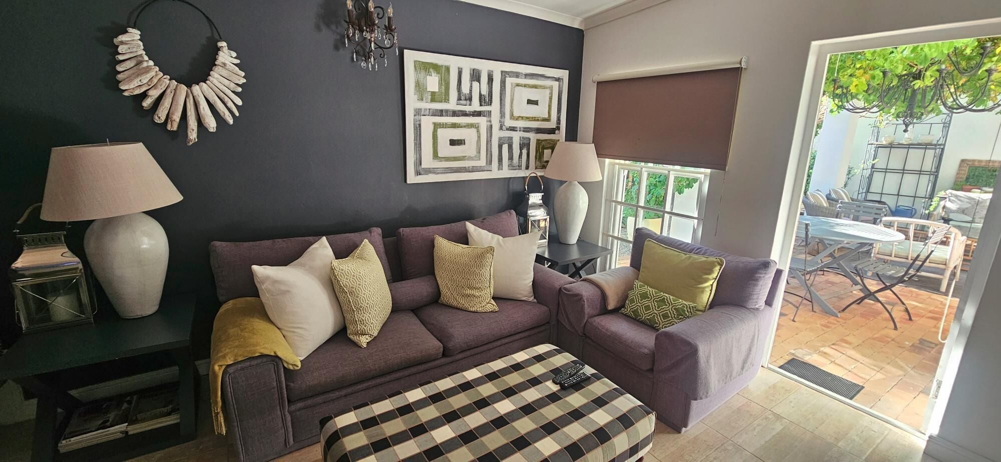 A living room with a sofa, two lamps, a checkered ottoman, and a wall with abstract art.