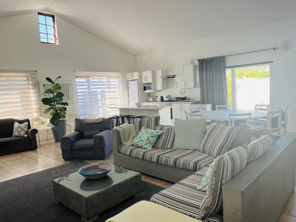 Una sala de estar moderna con un sofá, un sillón y una mesa de centro. Cuenta con una zona de cocina con armarios y una ventana.