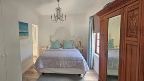 Un dormitori amb un llit, una làmpada de cristall, un quadre i un armari de fusta.