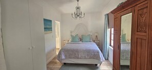 A bedroom with a bed, a chandelier, a painting, and a wooden wardrobe. - The Lily House Hermanus (Hermanus)