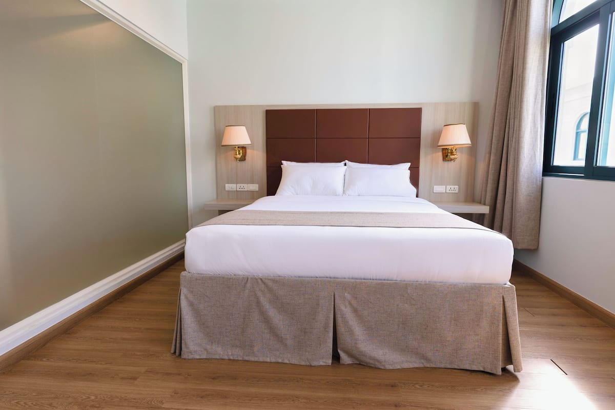 Habitación de hotel con una cama grande, dos lámparas de noche, un cabecero de madera y una ventana con cortinas.