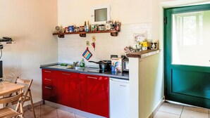 A kitchen with red cabinets, a sink, a stove, and a microwave. There is a wooden table and chairs, and a window with a view of greenery. - Casetta di Denise by Interhome (Imperia)