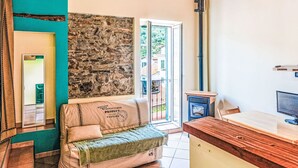 A cozy room with a stone wall, a wooden ceiling, a sofa, a small table, and a door leading outside. - Casetta di Denise by Interhome (Imperia)