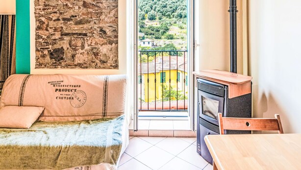 A room with a bed, a table, a chair, a fireplace, a stone wall, and a balcony with a view of a hillside. - Casetta di Denise by Interhome (Imperia)