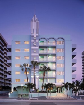 Een hotel met meerdere verdiepingen, balkons, palmbomen en een opvallende art-deco gevel.