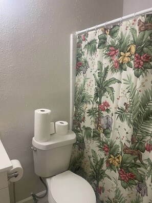 Ein Badezimmer mit Toilette, einer Duschvorhang mit Blumenmuster und zwei Toilettenpapierrollen an der Wand.