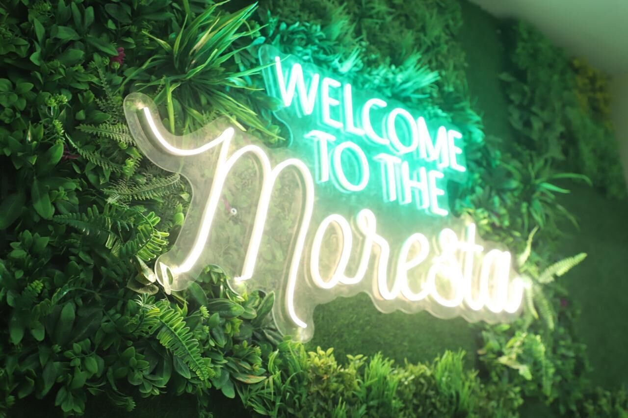 Un letrero de neón con el texto 'WELCOME TO THE MERESTIN' sobre un fondo de follaje verde.