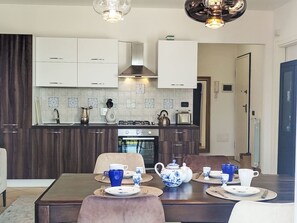 A modern kitchen with white cabinets, a gas stove, and a microwave. There is a dining area with a table set for two, featuring blue and white tea sets. - Apartment Melba by Interhome (Civezza)