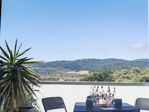 A terrace with a table, chairs, a potted plant, and a view of a hilly landscape. - Apartment Melba by Interhome (Civezza)