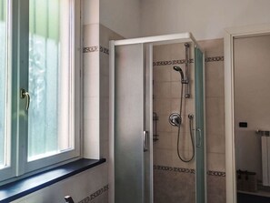 A bathroom with a glass-enclosed shower, a window with frosted glass, and a tiled wall with a decorative border. - Apartment Melba by Interhome (Civezza)