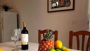 Mesa de jantar com garrafa de vinho, copos e uma tigela de frutas.