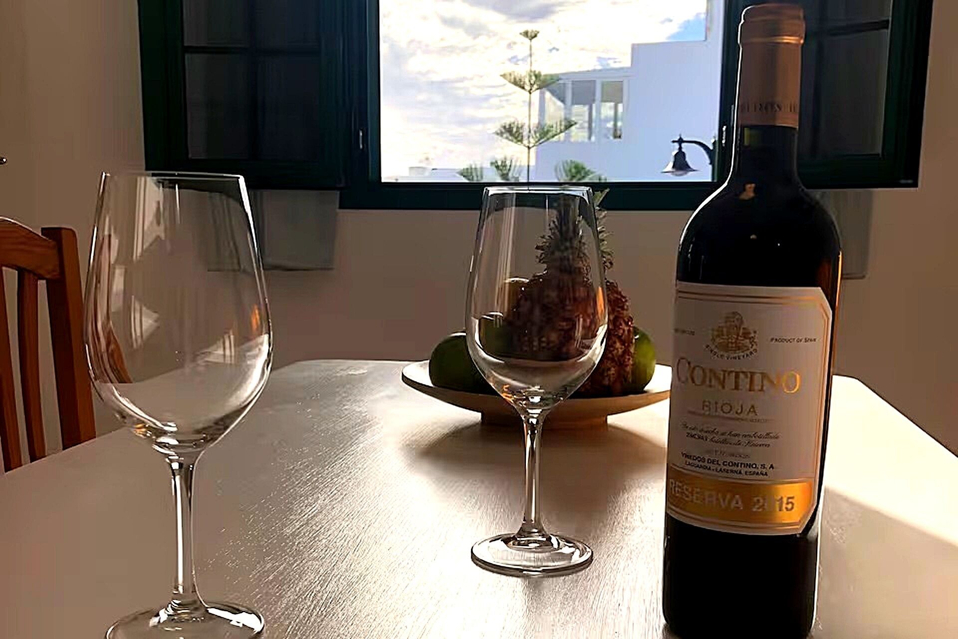 Una botella de vino Rioja Contino y dos copas de vino vacías sobre una mesa junto a una ventana.