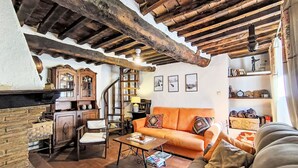 Un interno rustico caratterizzato da travi a vista in legno, un camino in pietra, un armadietto in legno, un divano e un tavolino con un libro.