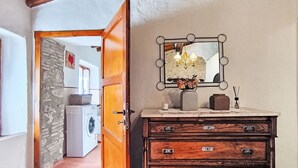 Un corridoio con una porta in legno, una lavatrice, un settimino con cassetti e uno specchio illuminato.