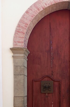 A red wooden door with a metal plaque reading 'CASA' and a brick archway.