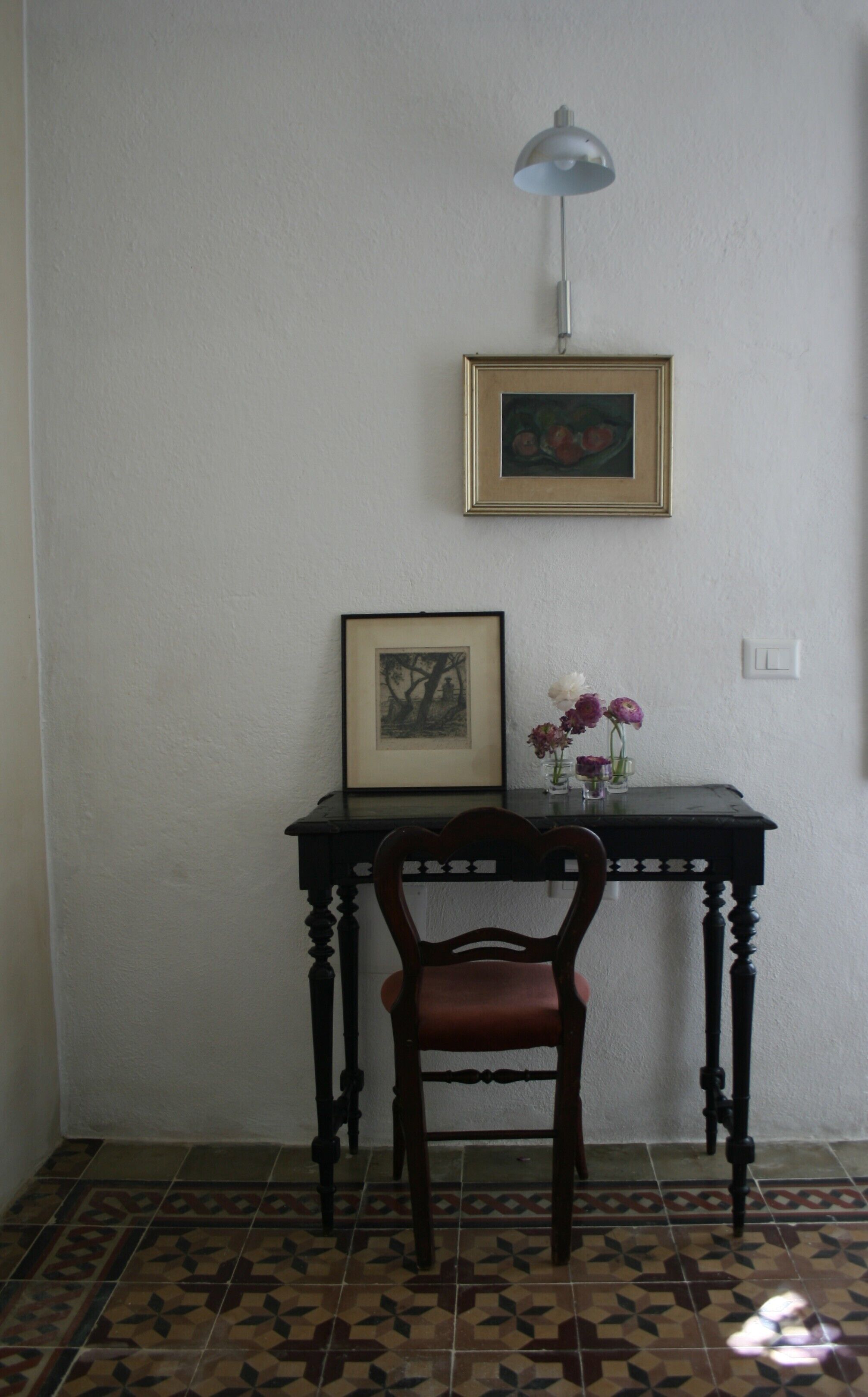 Une pièce comprenant un bureau, une chaise, un tableau encadré et une lampe.