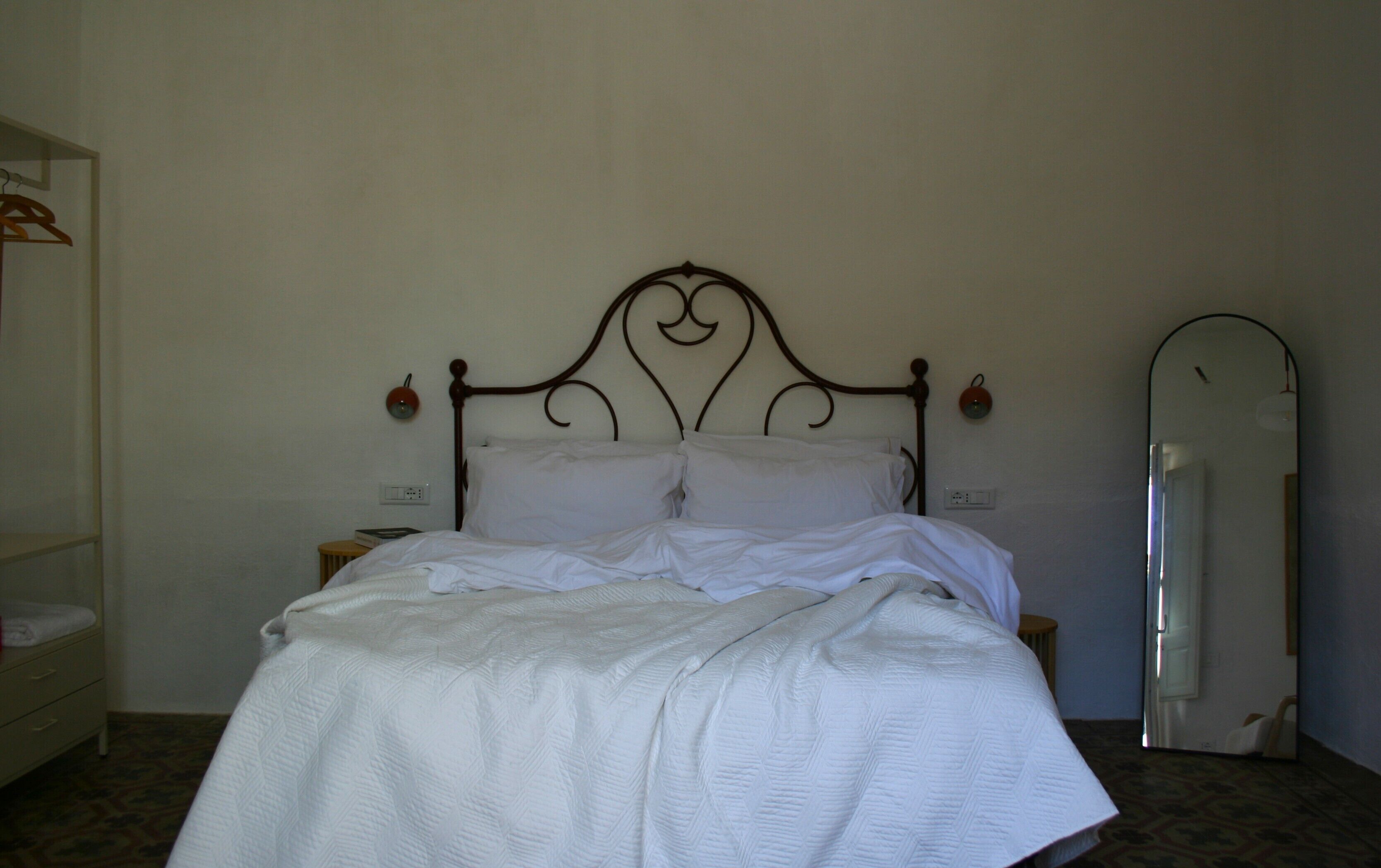 A neatly made bed with a headboard, a bedside table with a lamp, and a mirror on the wall.