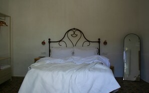 Una cama bien hecha con cabecera, una mesita de noche con lámpara y un espejo en la pared.