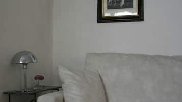 Una habitación con un sofá blanco, una mesita de noche con lámpara y un cuadro en la pared.