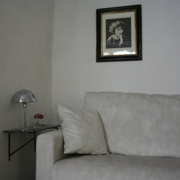 A room with a white sofa, a small side table with a lamp, and a framed picture on the wall.