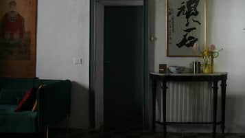 Una habitación con una puerta cerrada, un cuadro caligráfico enmarco, una pequeña mesa con un florero y un cojín sobre un sofá verde.