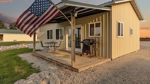 A single-story building with a covered patio, a grill, and an American flag. - The Goose Cabin | 5-Cabin Compound, Sleeps 30 (Decatur)