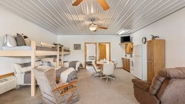 A room with bunk beds, a desk, a chair, a sofa, and a ceiling fan. - The Goose Cabin | 5-Cabin Compound, Sleeps 30 (Decatur)