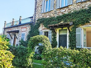 Ein Steinhaus mit Efeu, Fensterläden und einem Balkon.