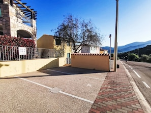 Ein Parkplatz mit befestigter Oberfläche, einem Pflasterweg und einem Gebäude mit steinverkleidetem Mauerwerk und einem Metallzaun.