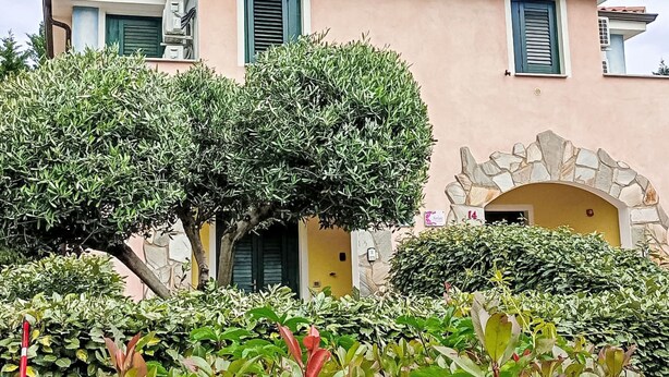 Un edificio con un arco in pietra, una facciata rosa e persiane verdi.