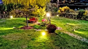Un giardino ben illuminato con una panchina rossa, alberi e una collina sullo sfondo.
