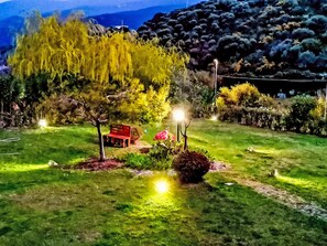 Ein gut beleuchteter Garten mit einer roten Bank, Bäumen und einer Hügelkulisse im Hintergrund.