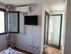Ein Zimmer mit einem Bett, einem Fernseher, einer Klimaanlage und einer Tür zu einem anderen Raum.