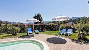 Una piscina con lettini e ombrelloni, circondata da vegetazione e colline.