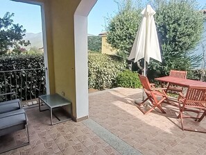 Eine Terrasse mit Tisch und Stühlen, einem weißen Sonnenschirm und Blick auf Grünflächen und Hügel.