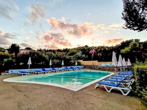 Ein rechteckiger Pool mit blauen Liegestühlen und weißen Sonnenschirmen darum herum.