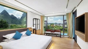 Quarto de hotel moderno com uma cama grande, TV, varanda com vista para montanhas e uma escrivaninha com abajur.