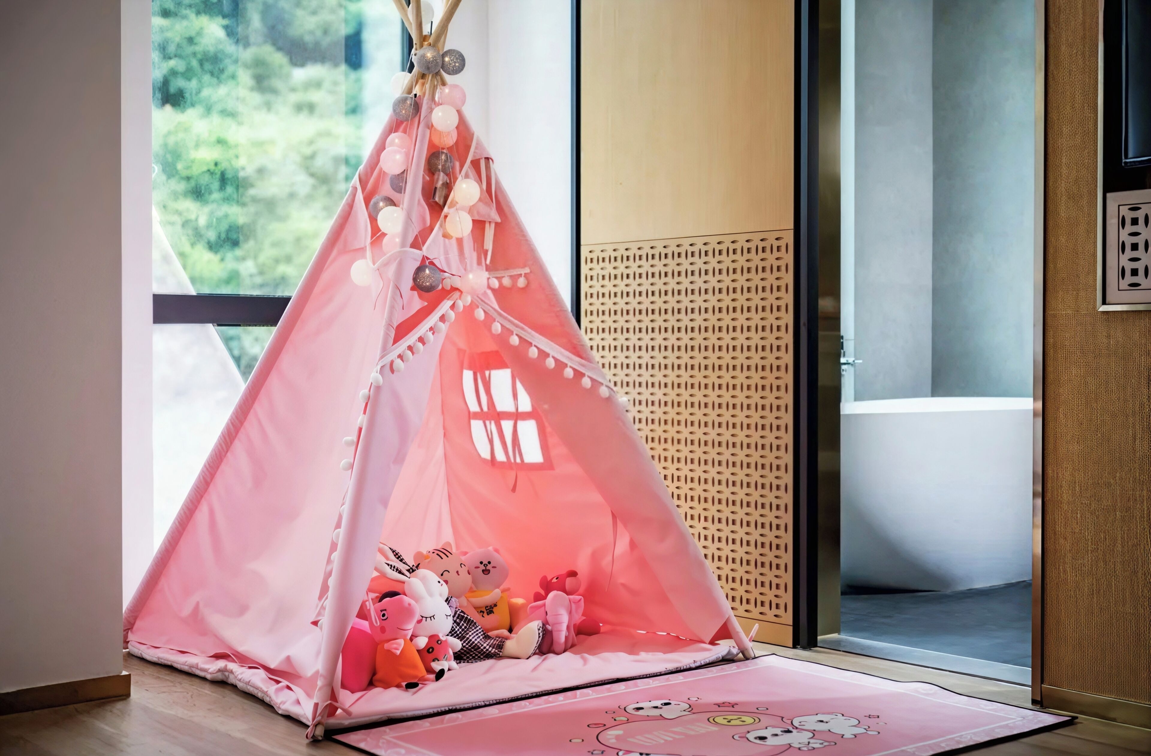 Uma tenda rosa para brincar com brinquedos por dentro, uma janela com vista para o verde, e uma parede de treliça de madeira.