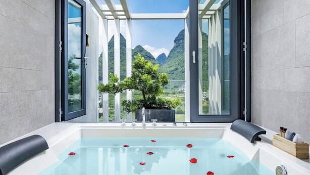 Casa de banho moderna com banheira de hidromassagem envidraçada, uma planta em vaso e vista para as montanhas.