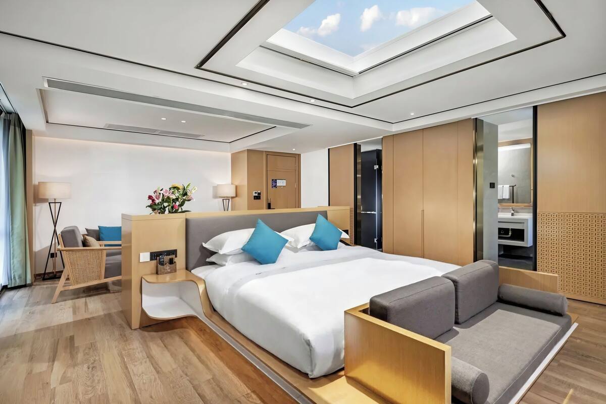 Una habitación de hotel moderna con tragaluz, una cama grande, un sofá, una mesita de noche y un armario.