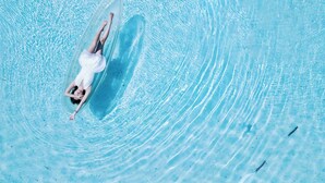 Uma pessoa deitada em uma prancha de surf em uma piscina azul cristalina.