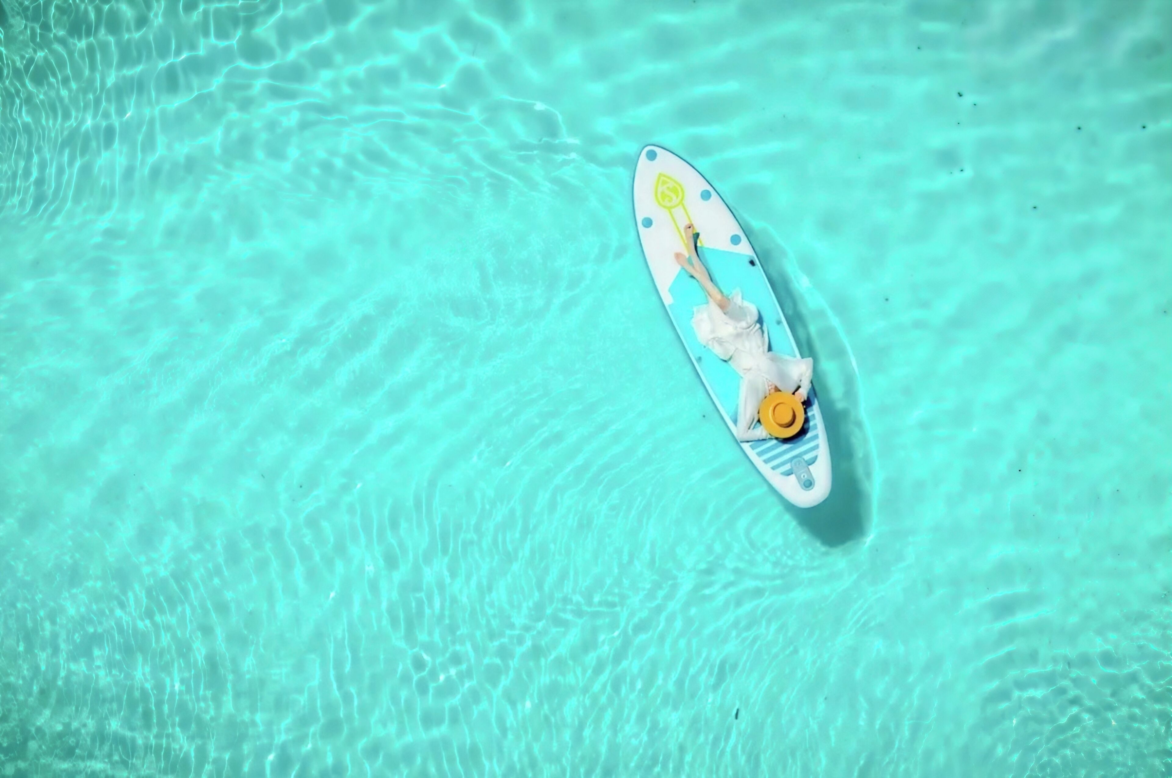 A person lying on a surfboard in clear turquoise water.