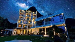 Um hotel moderno de vários andares com fachada de vidro ampla, entrada bem iluminada e vista para o céu noturno.