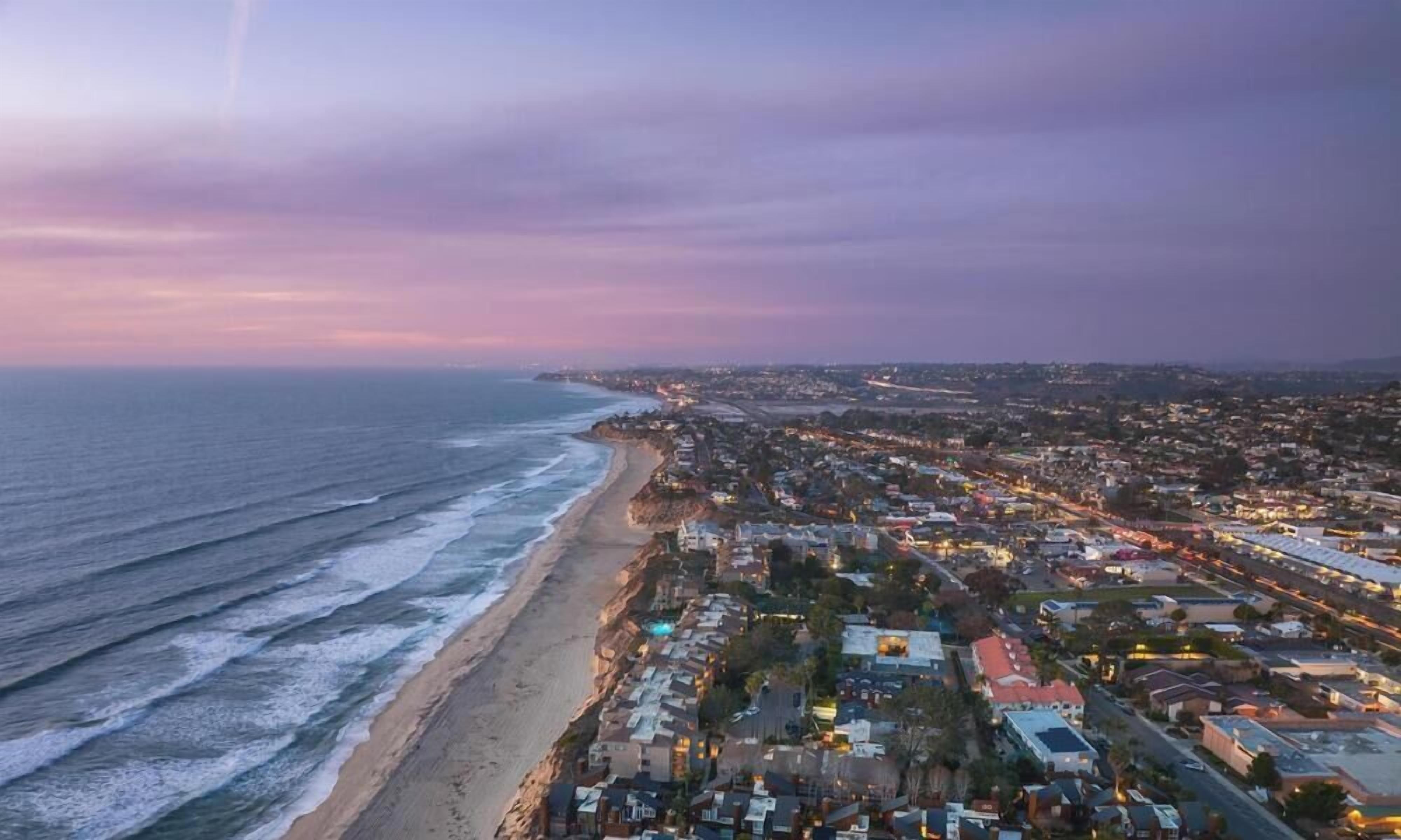 A coastal cityscape with a beach, residential buildings, and a distant view of the ocean.