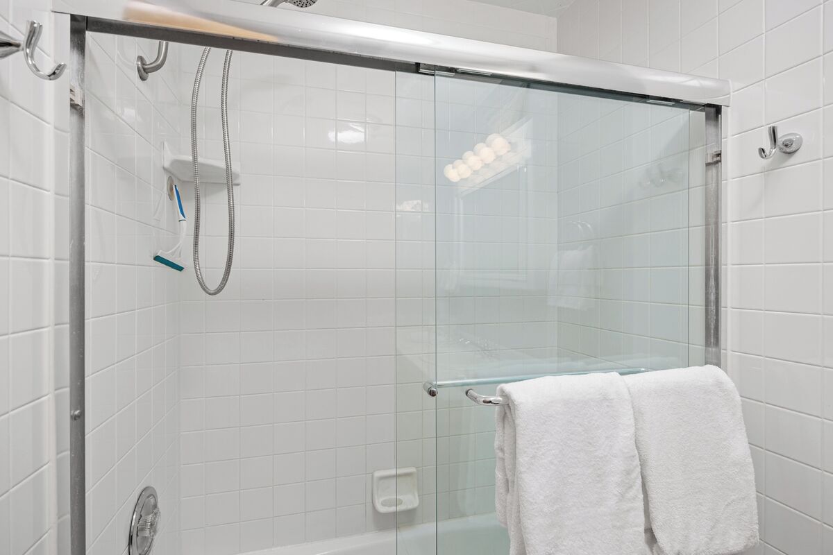 Une douche fermée par des parois de verre, avec une porte en verre, une serviette blanche accrochée à la poignée de la porte et un mur recouvert de carreaux blancs.